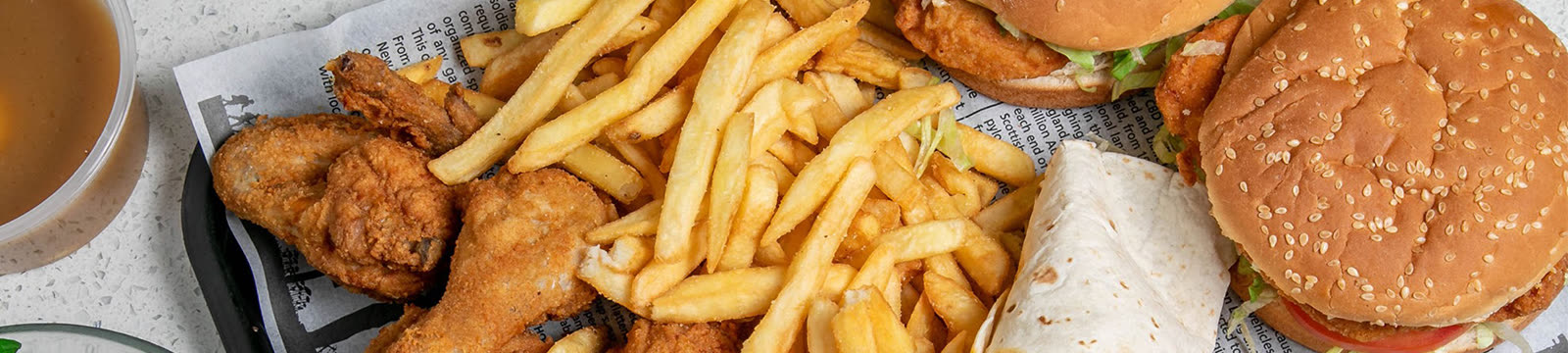 Bovenaanzicht van friet, gefrituurde kip, een wrap en twee burgers op krantenpapier.