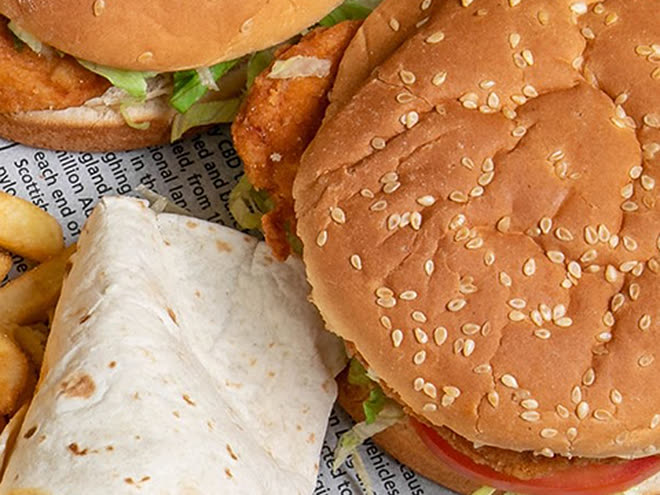 Een wrap en een burger met sesamzaad, naast wat friet op krantenpapier.